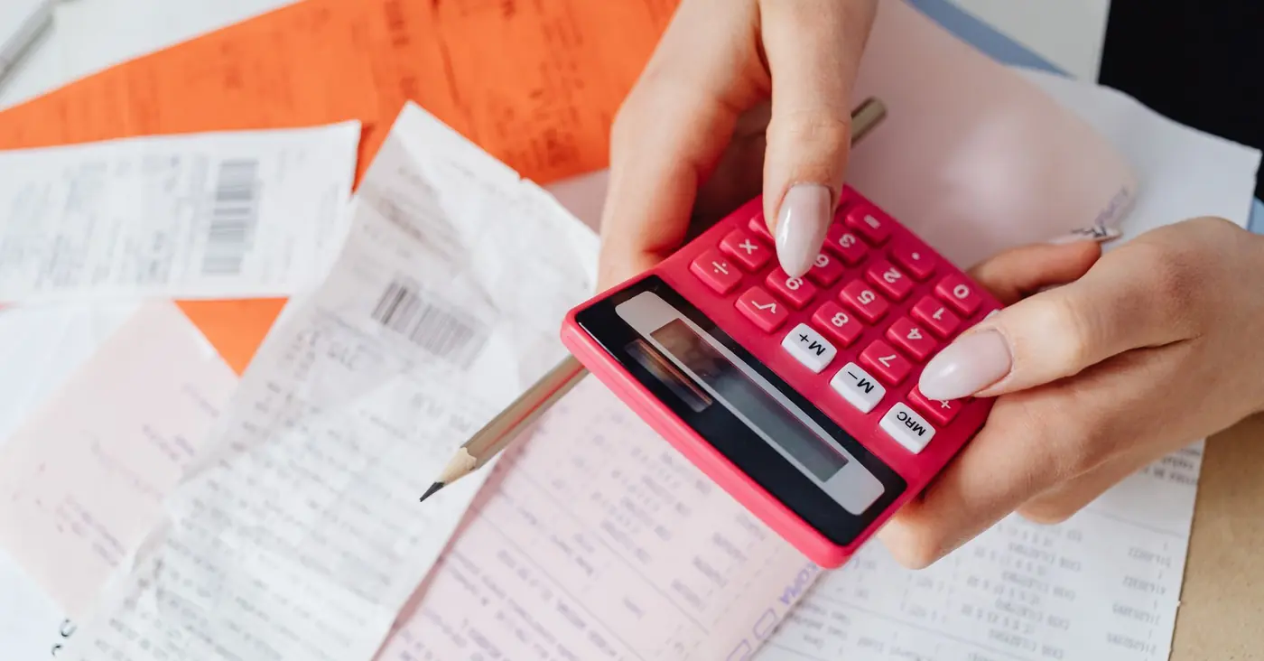 Une main tape sur une calculatrice posée sur des tickets et des factures