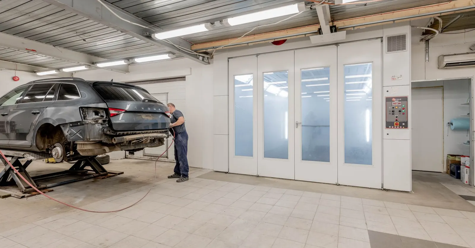 Atelier de carrosserie : un carrossier travaille sur un véhicule devant les cabines de peinture